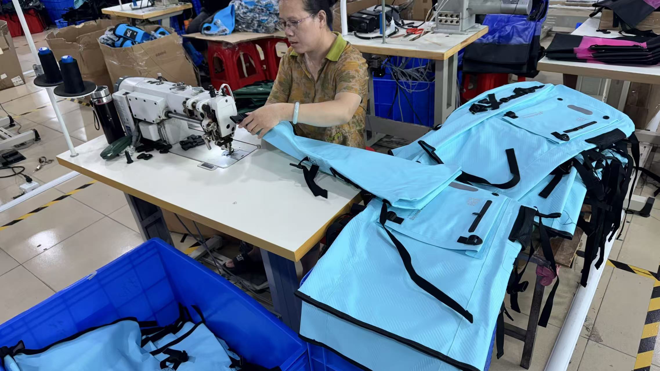 DryCross worker sewing components beside blue waterproof bag panels at a factory workstation